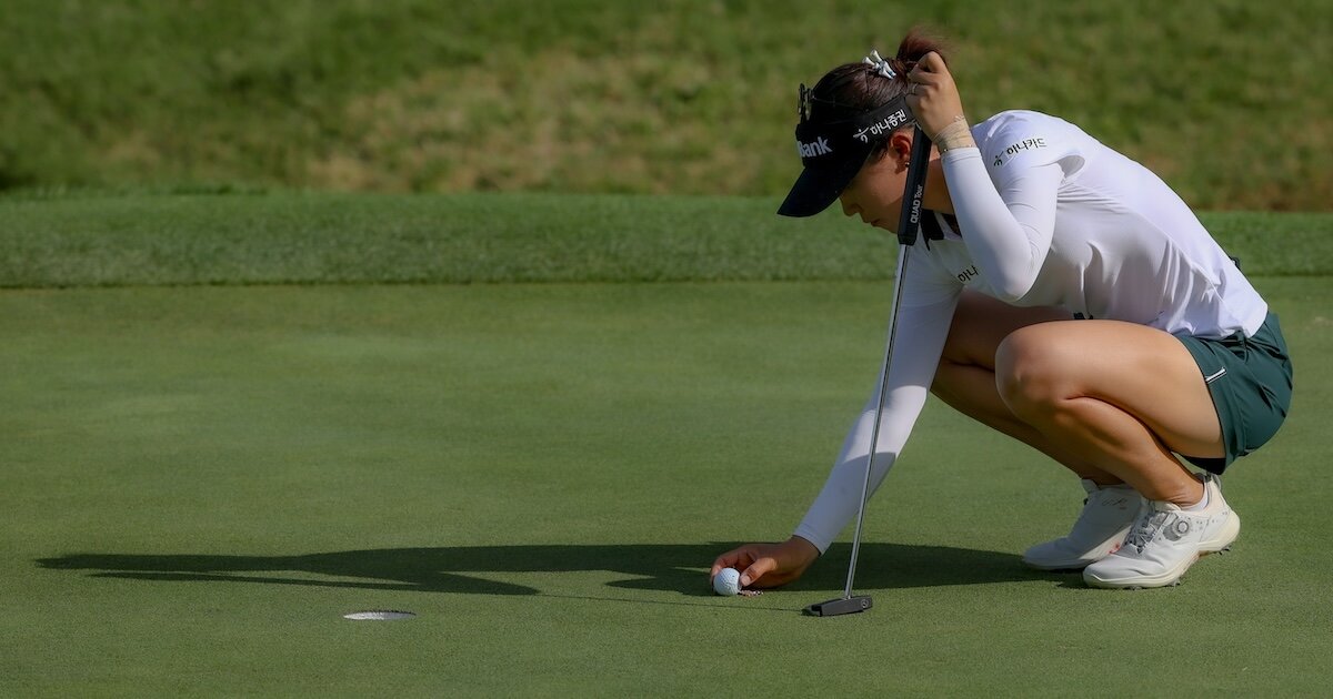 Golferin kniet auf dem Rasen und richtet einen Goldball aus